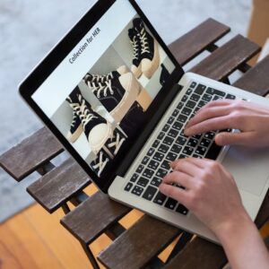 Hands browsing sneakers on laptop, showcasing online store shopping experience.